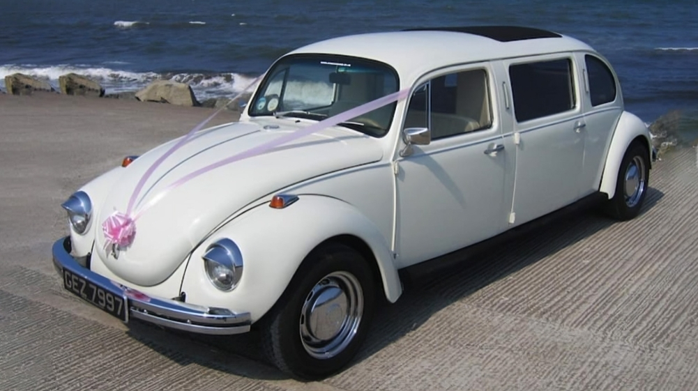 Ivory classic Beetle dressed with light pink ribbons and bow parked by the Yorkshire sea coast