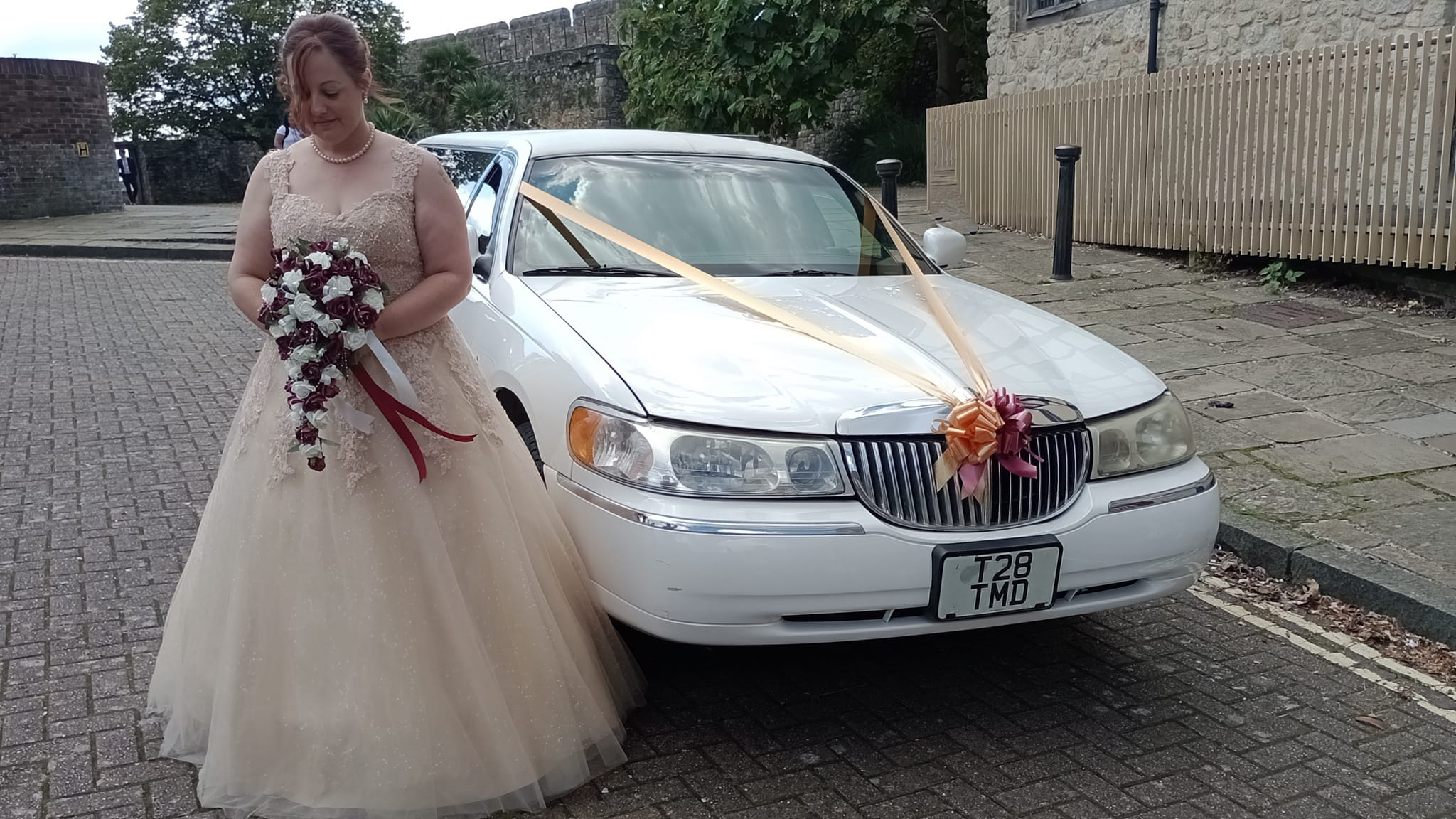 Bride wearing an Ivory dress and holding a bouquet of flowers standing next to a white stretched american limousine