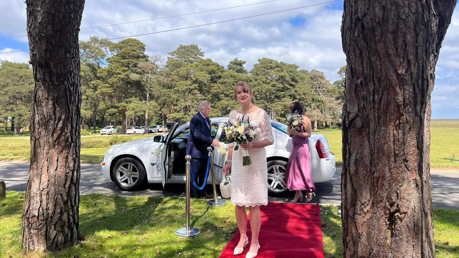 Bride and Bridesmaids standing on Red Carpet layed out on front of a Modern White Wedding Car