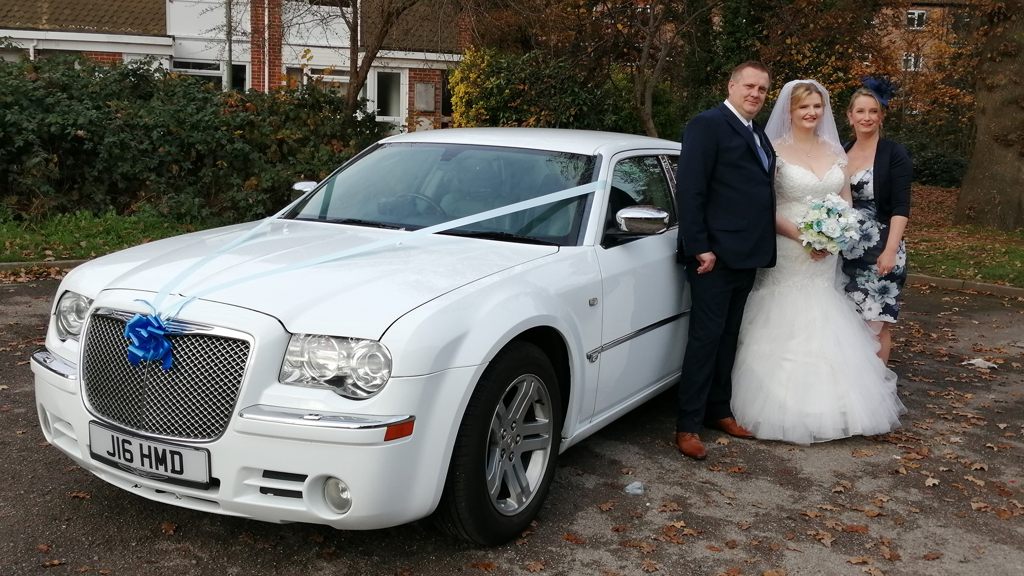 Bride and her parents standing by a Modern White Car decorated with royal blue ribbons