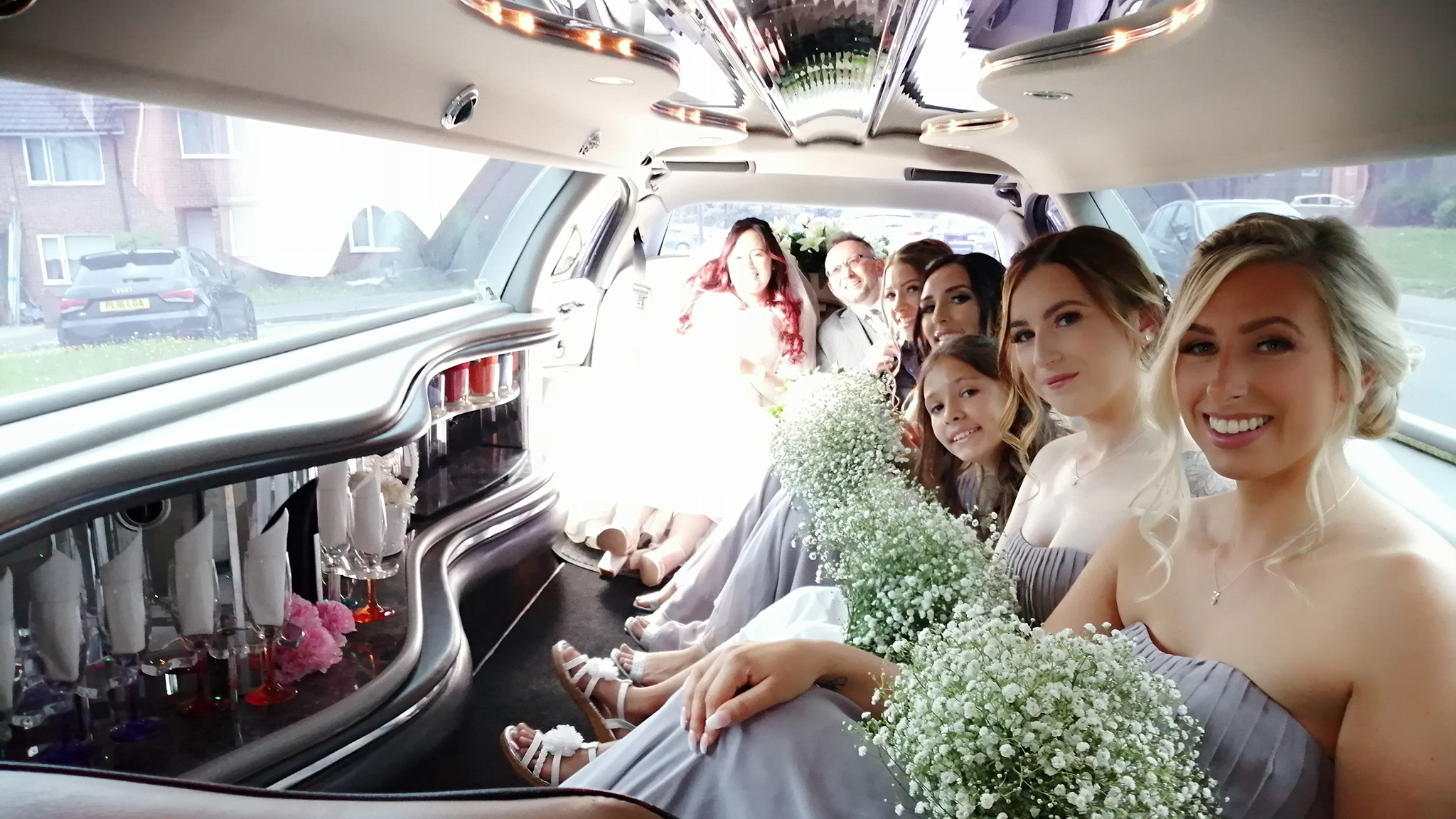 Bridesmaids smiling and holding some flowers inside a stretched limo