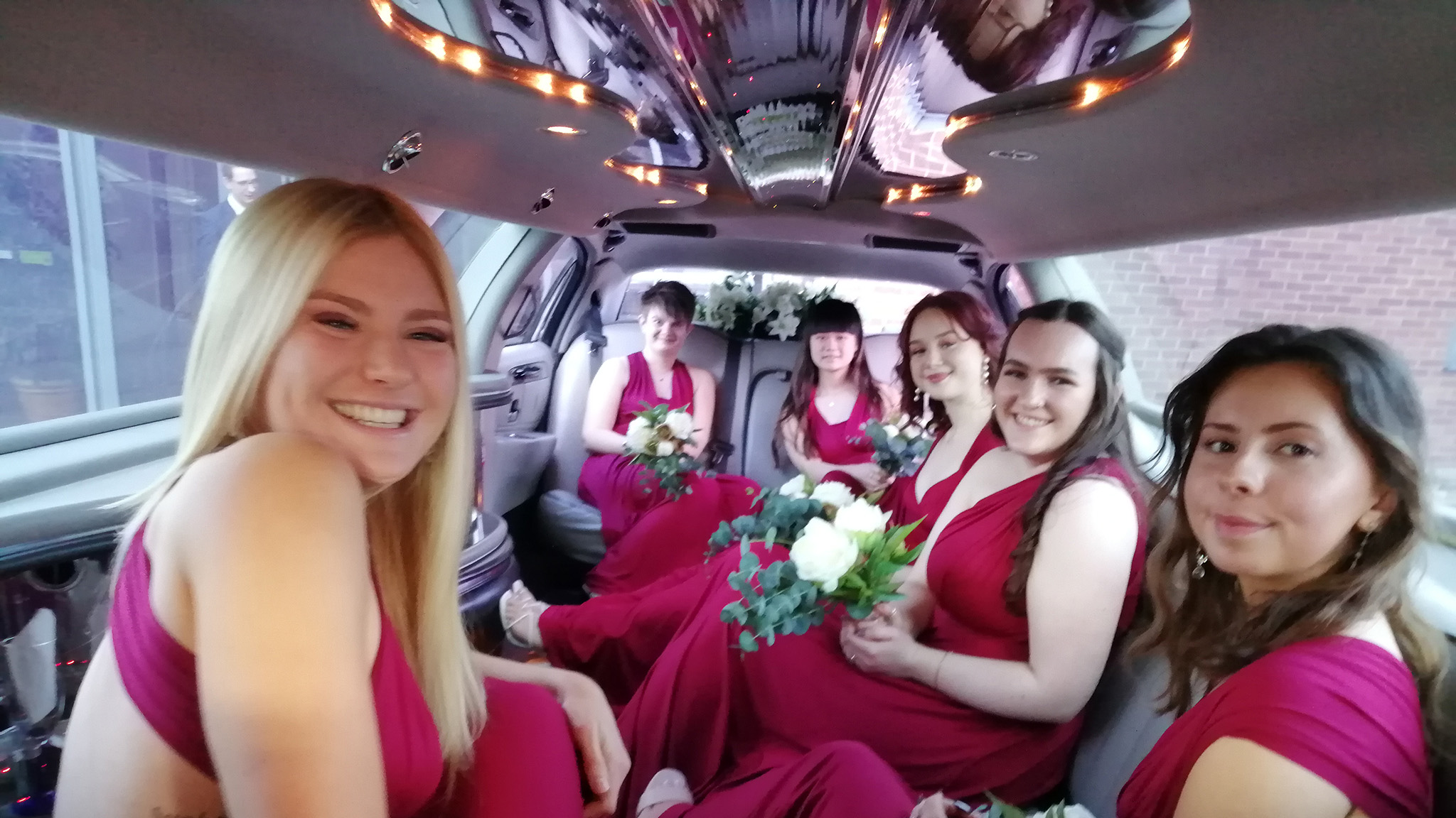 Bridesmaids wearing matching pink dresses seated inside a Stretched limousine