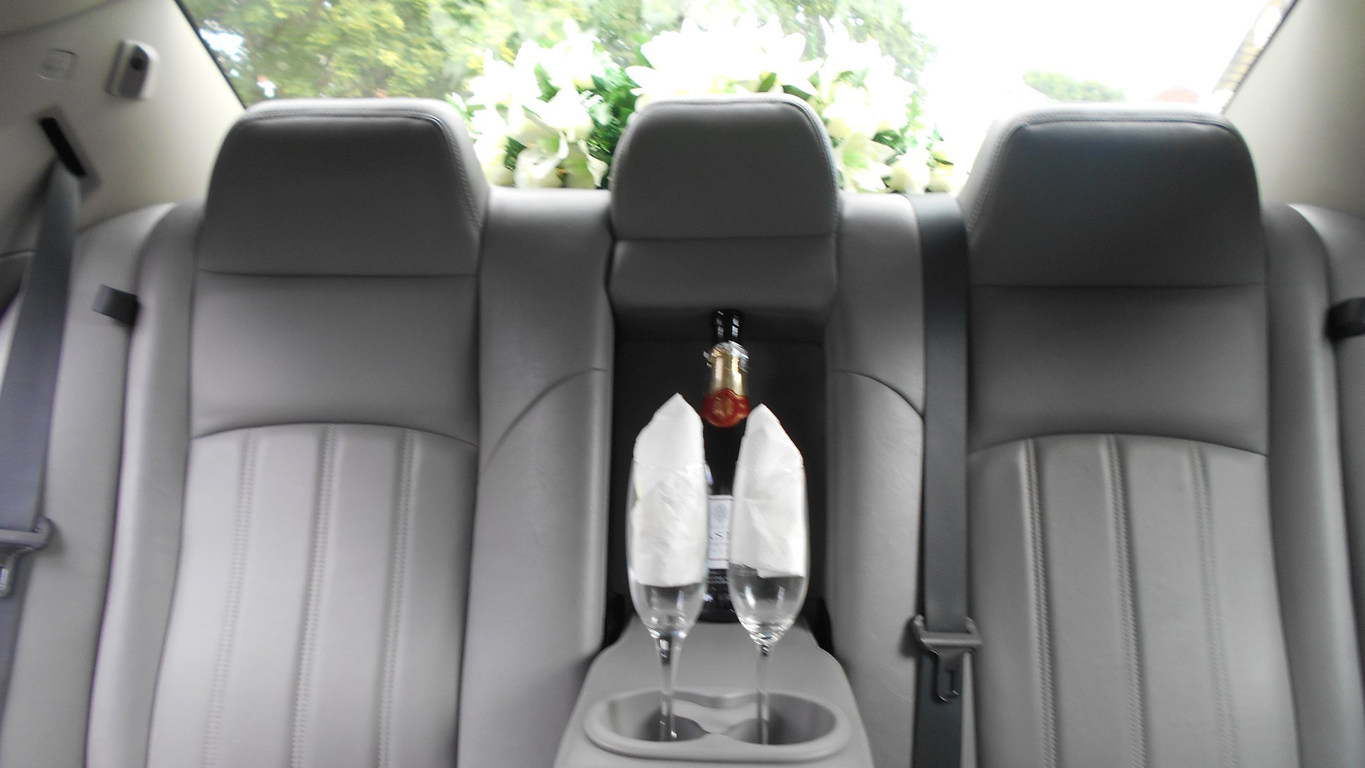 Rear seats inside a chrysler 300c car with a bottle of champagne and two glasses on the centre armrest.