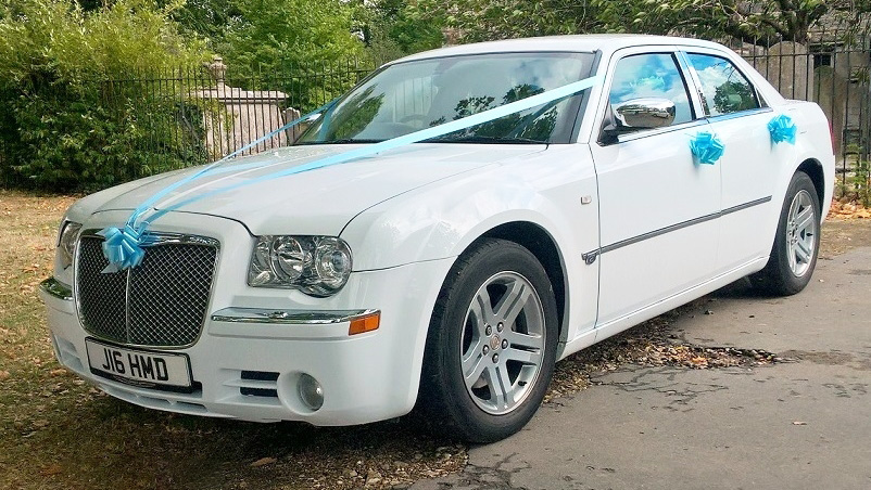 Lioght Blue ribbons and bows on front grill and door handles of a Modern White american Chrysler 300c saloon car