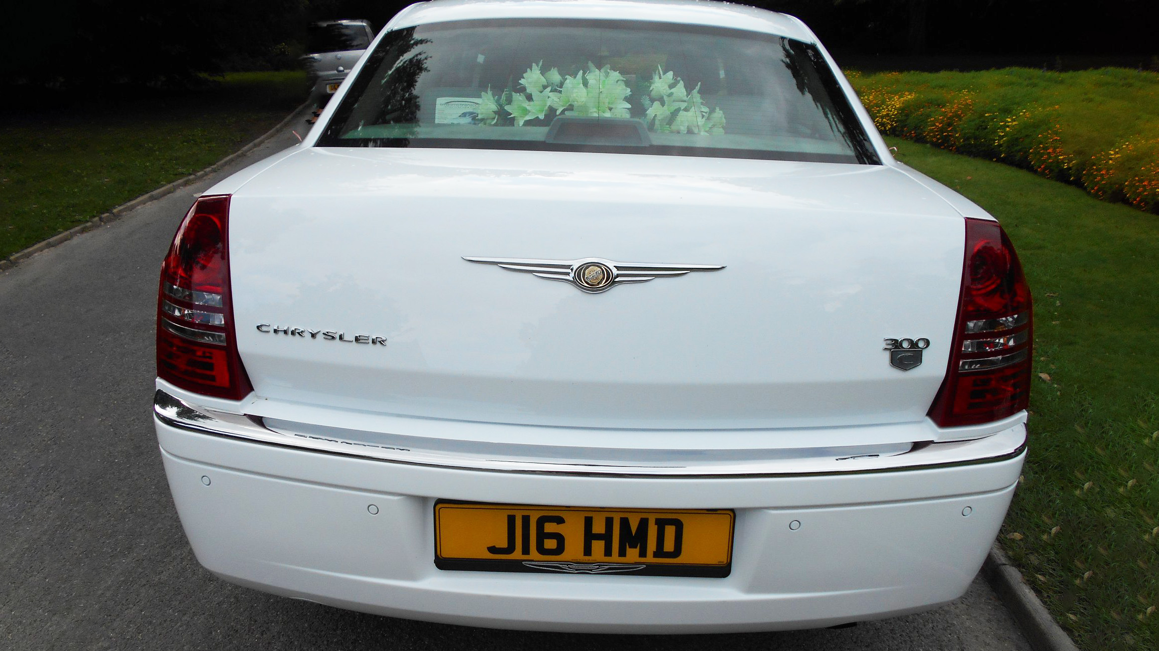 Rear view of a white Chrysler 300c Car with flowers on the rear parcel shelf.