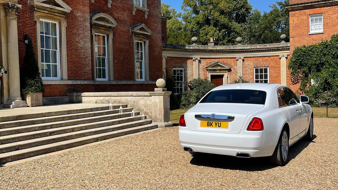 Rear view of white rolls-royce ghost parked in front of wedding venue