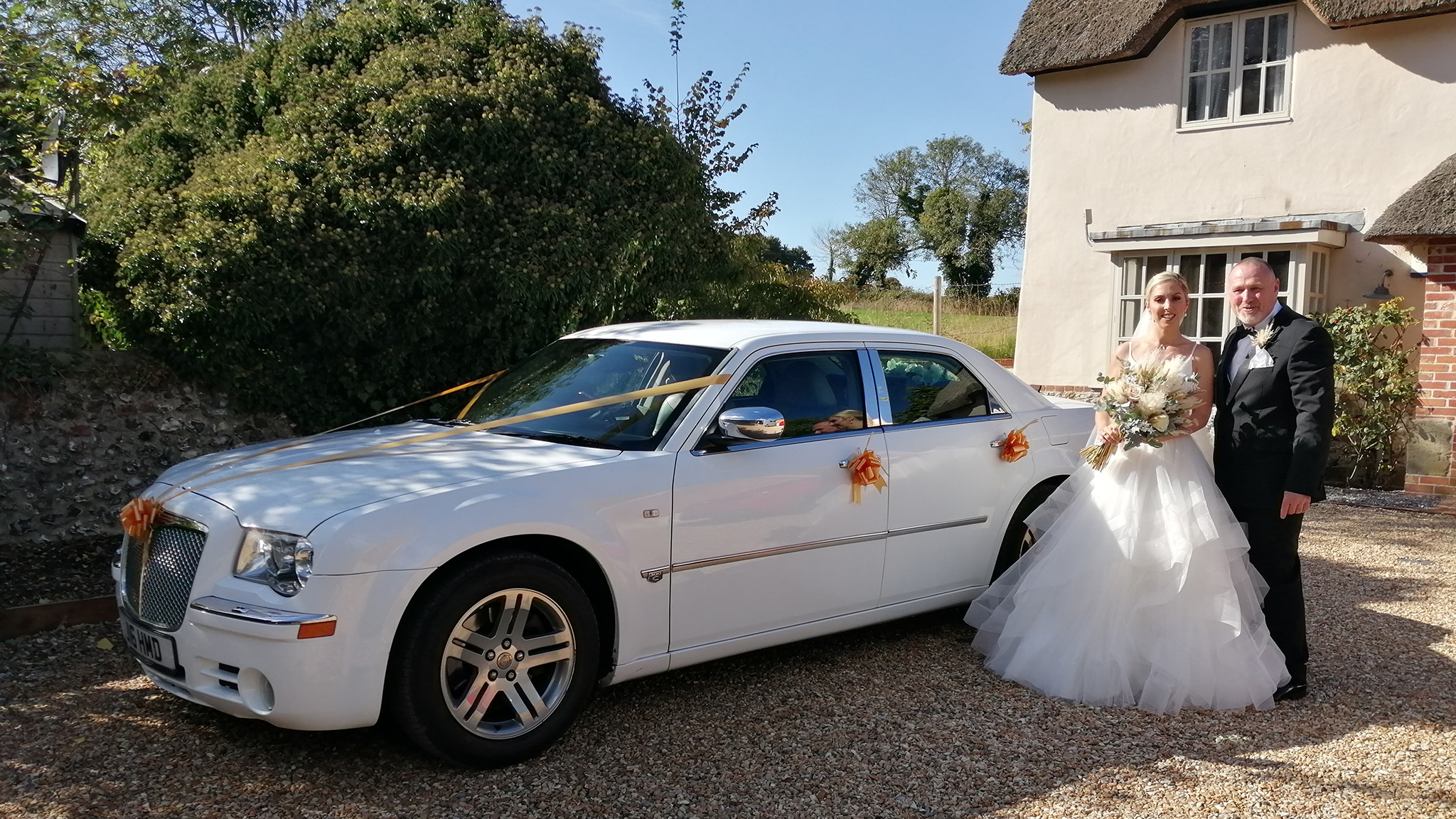 Bride and Groom standing by a white modern Chrysler 300c car decorated with orange ribbons