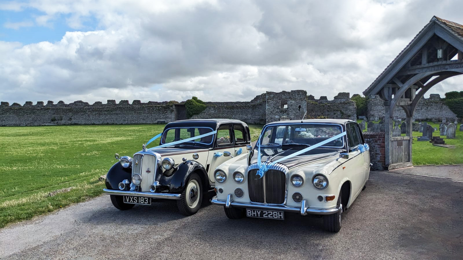 Classic Rolver parked next to a classic Limousine in matching black and White colours. Portschester Castle in shown in the background