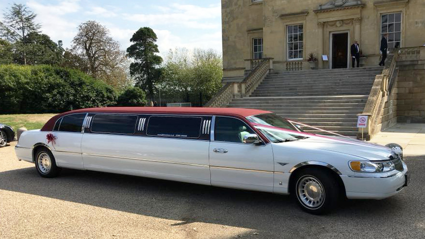 Right side view of white stretched limousine with burgundy roof parked in front of a wedding venue