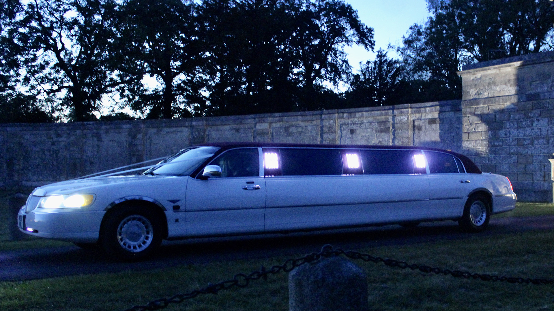 White stretched limousine at dusk with headlights on and side window lights on