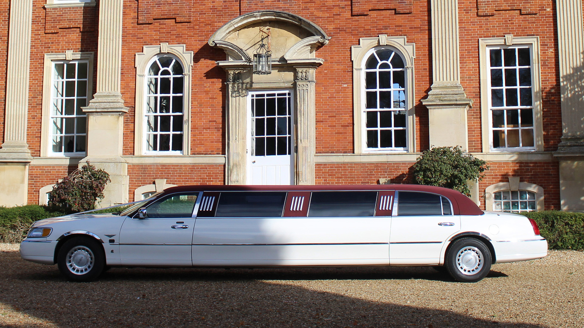 Right side view of a white stretched limousine with Burgundy roof