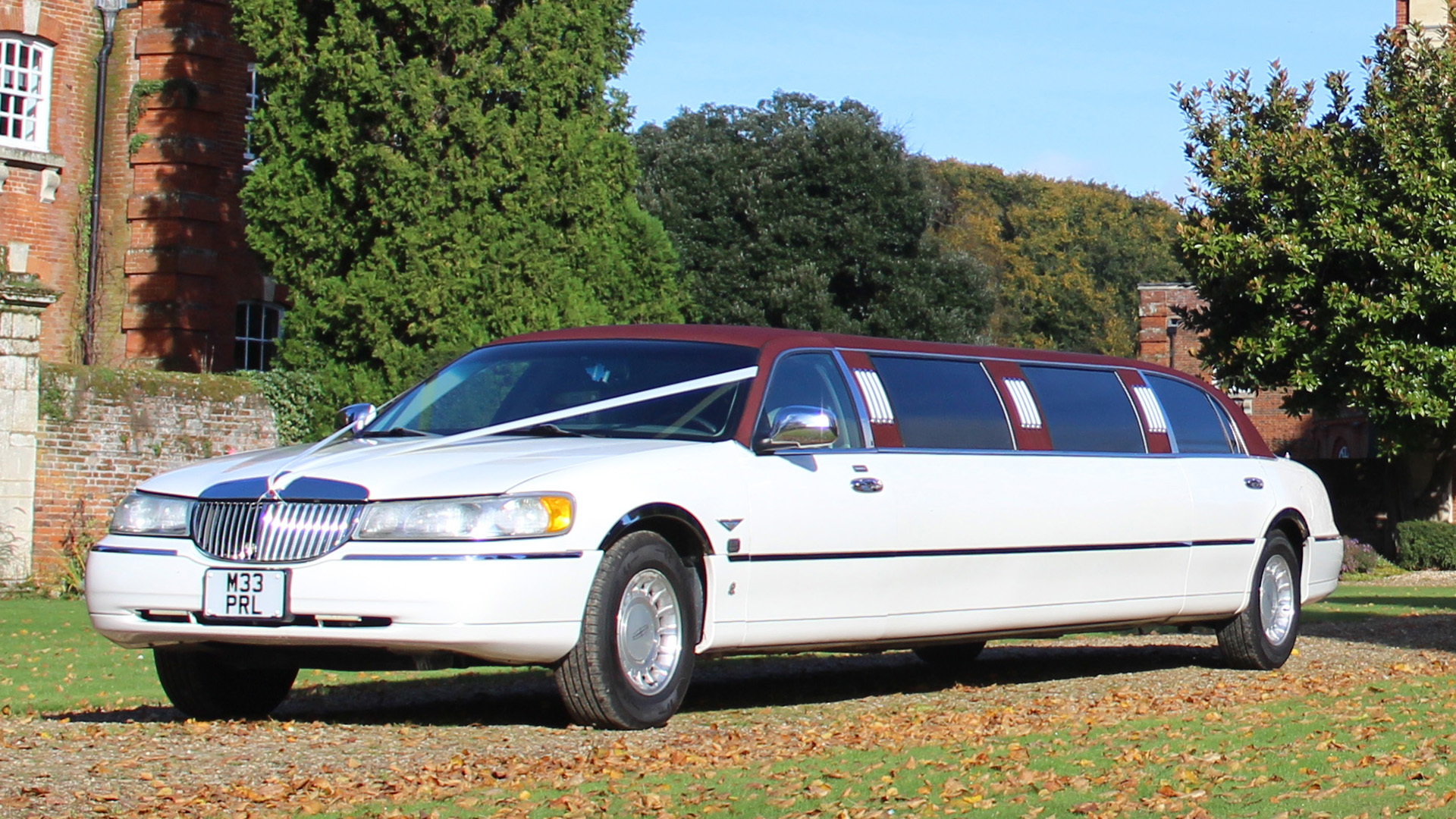 White stretched american limousine with Burgundy roof decorated with white wedding ribbons across bonnet