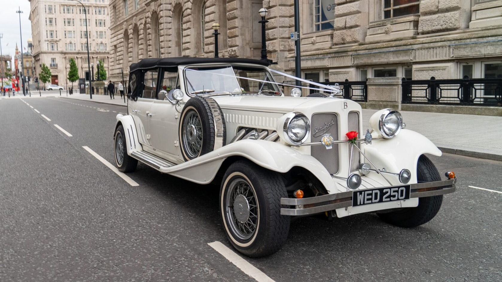 Ivory Beauford with a black soft top roof dressed with white wedding ribbons parked in the street of Liverpool