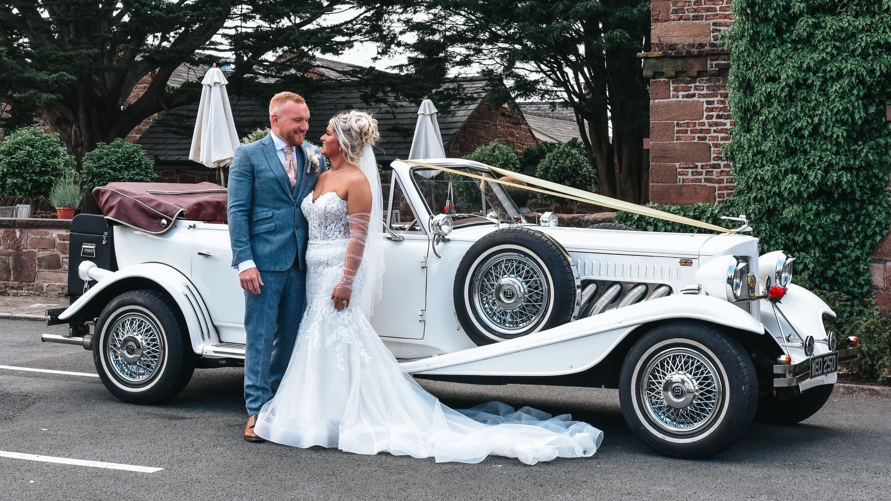 Bride wearing a white wedding dress with groom in a Turquoise Blue suit standing in front of a Vintage Beauford