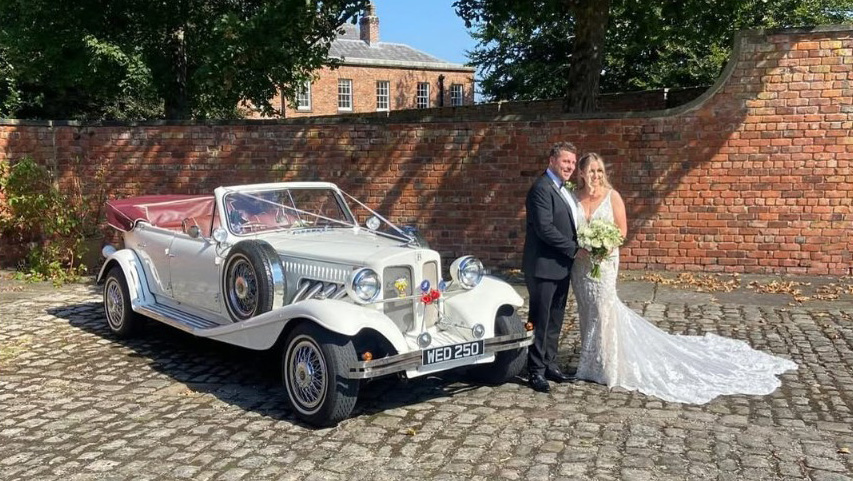 Bride and Groom standing by a Vintage Beauford decorated with wedding ribbons with roof open