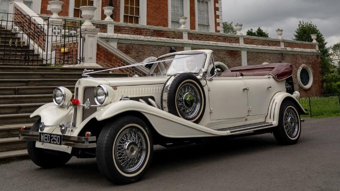 30s vintage style Beauford in a Cream colour with soft top roof down parked in frotn of a wedding venue in Liverpool