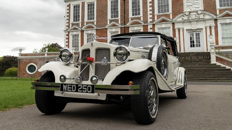 Frotn view of Beauford Wedding car in Old English white with black soft top roof and spare wheel mounted on the side of the vehicle