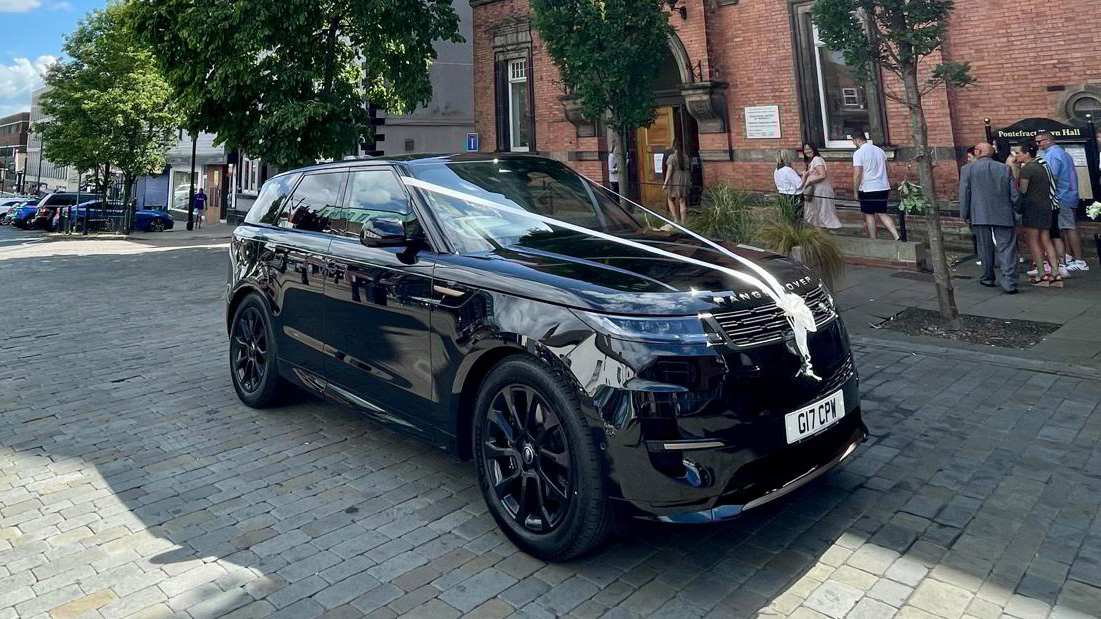 Black Range Rover with black alloy wheels dressed with white wedding ribbons parked in front of Pontefract Toan Hall in Yorkshire