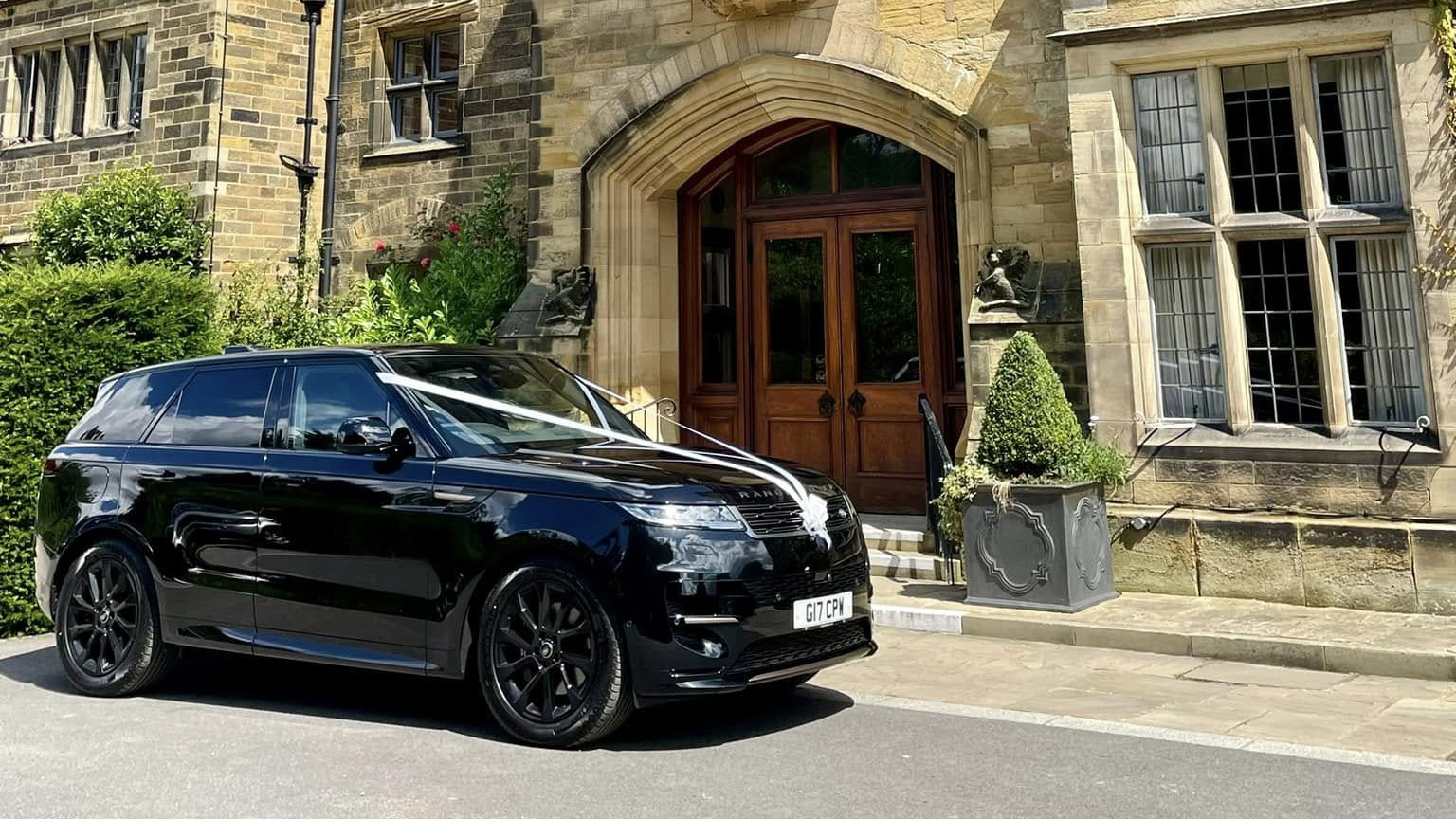 Right side view of a modern black range rover with white wedding ribbons in front of a wedding venue