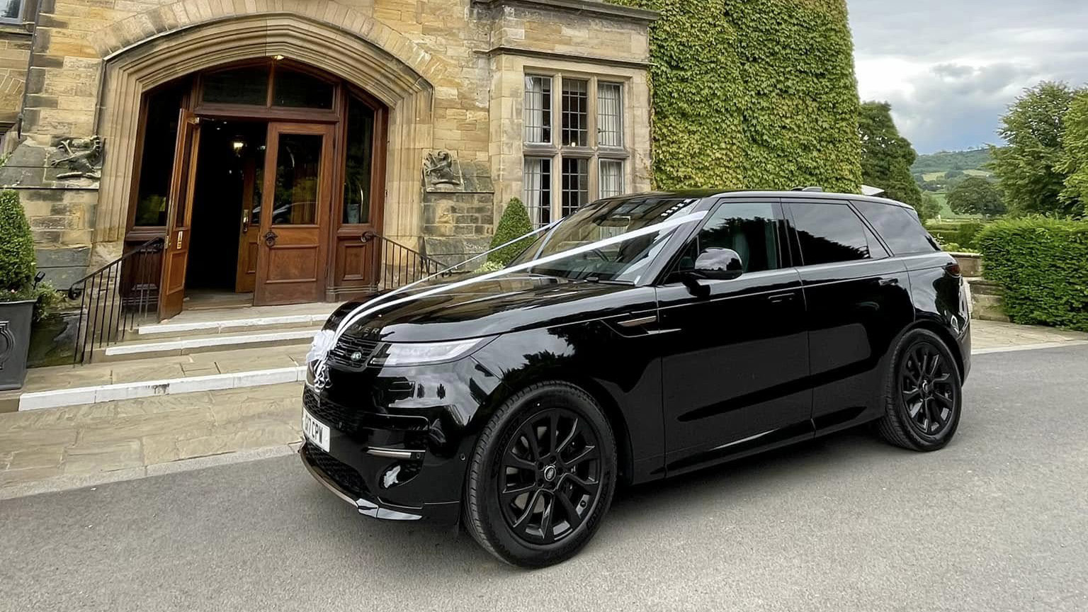 Left side view of a modern black range rover with white wedding ribbons and black alloy wheels