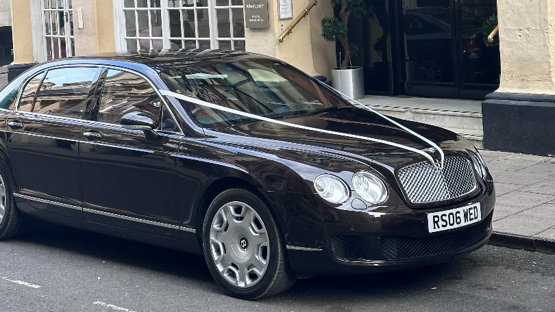 Modern Black Bentley Flying Spur decorated with white ribbons parked in front of a venue in Swindon