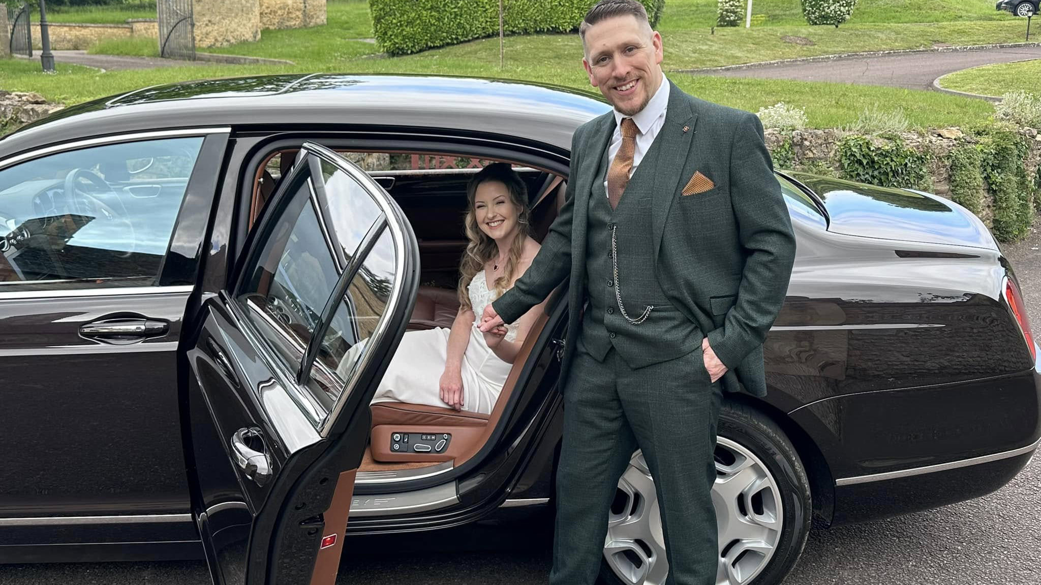 Groom opening the rear passenger side door to the Bride wearing a white dress