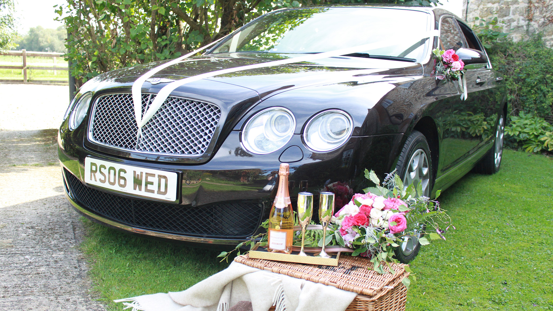 Black Bentley Flying Spur with Champagne bottle and glass on a hamper in front of the vehicle