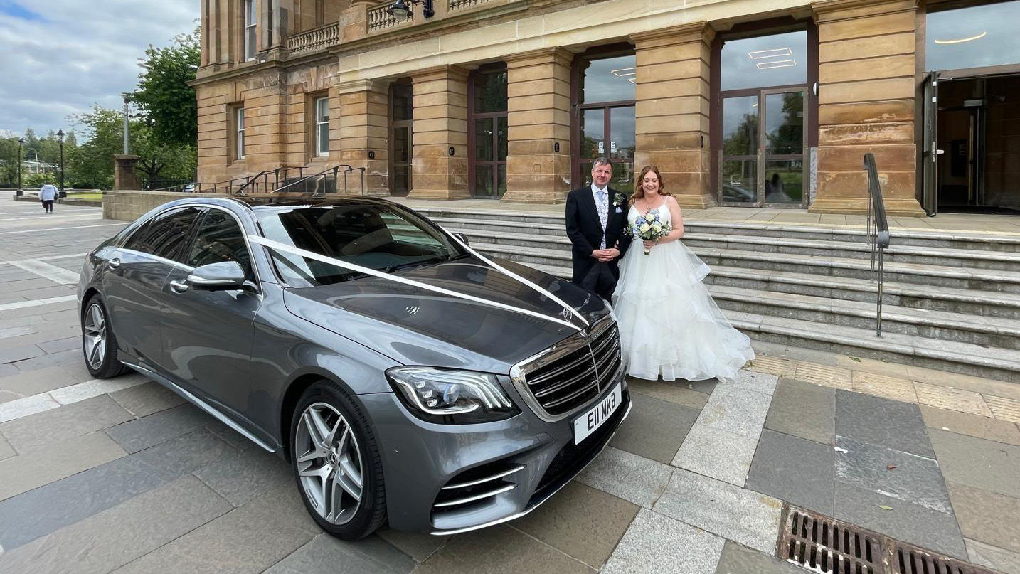 Bride and Groom standing by a Modern Mercedes in Grey with White wedding ribbons