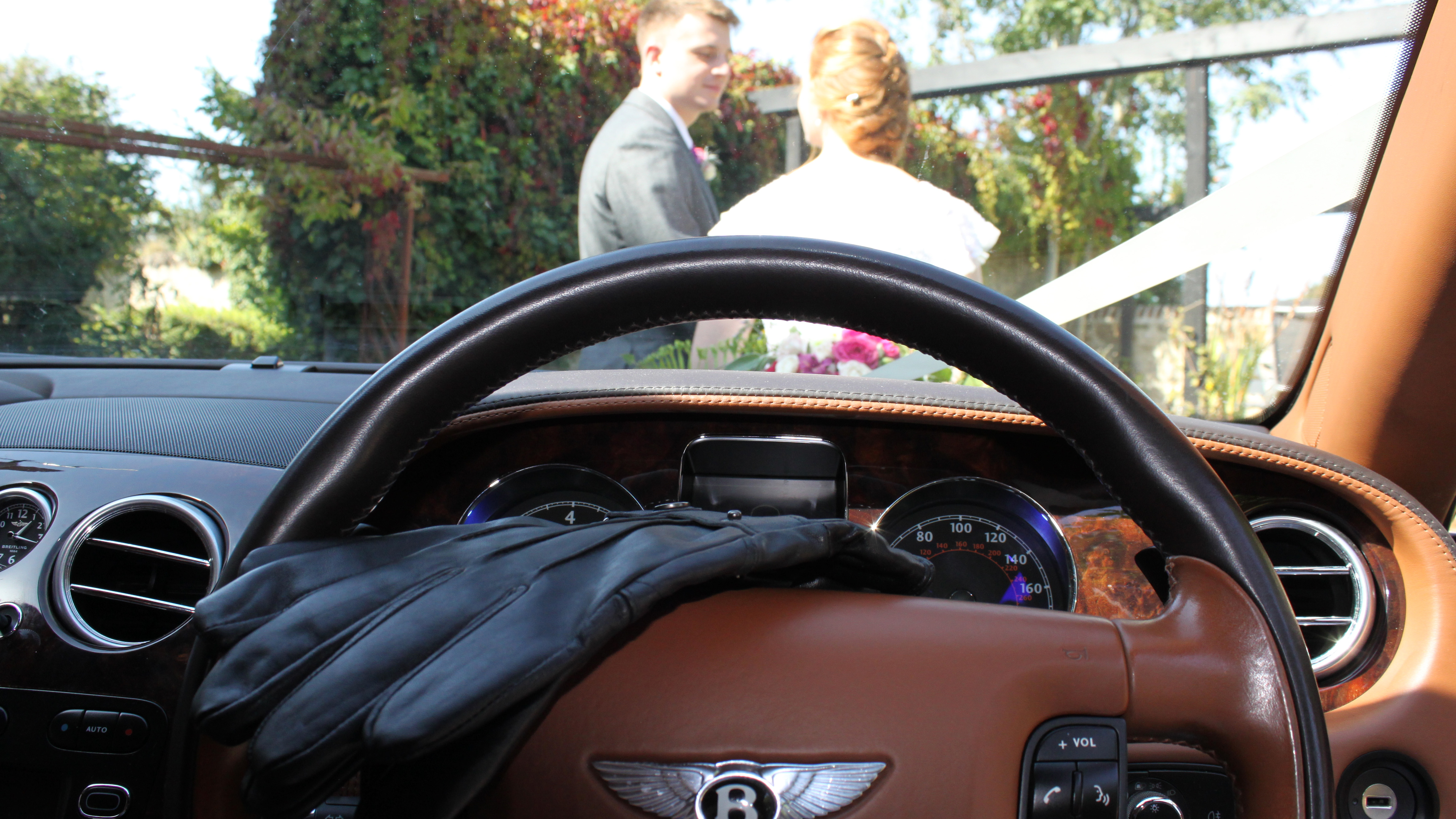 Front driver dashboard and steering wheel with pair of black gloves. Bride and groom can be seen through the front window.