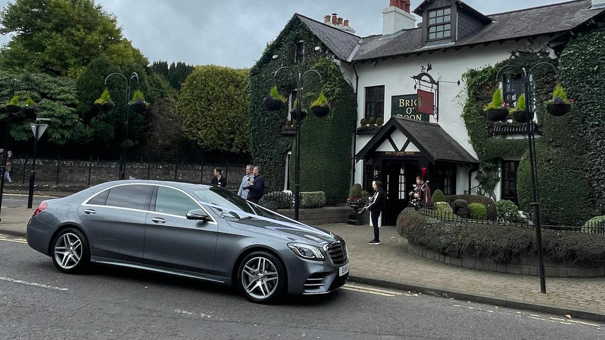 Mercedes with white ribbons parked in front of a wedding venue