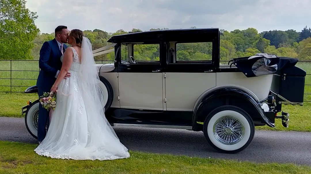 Bride and Groom kissing in front of an Imperial vintage car with convertible roof down