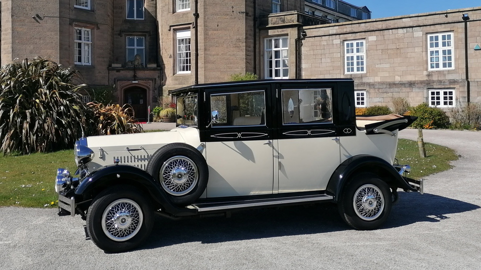 Left side view of a Black and Ivory Imperial wedding car with convertible roof down parked in front of Leasowe Castle Hotel