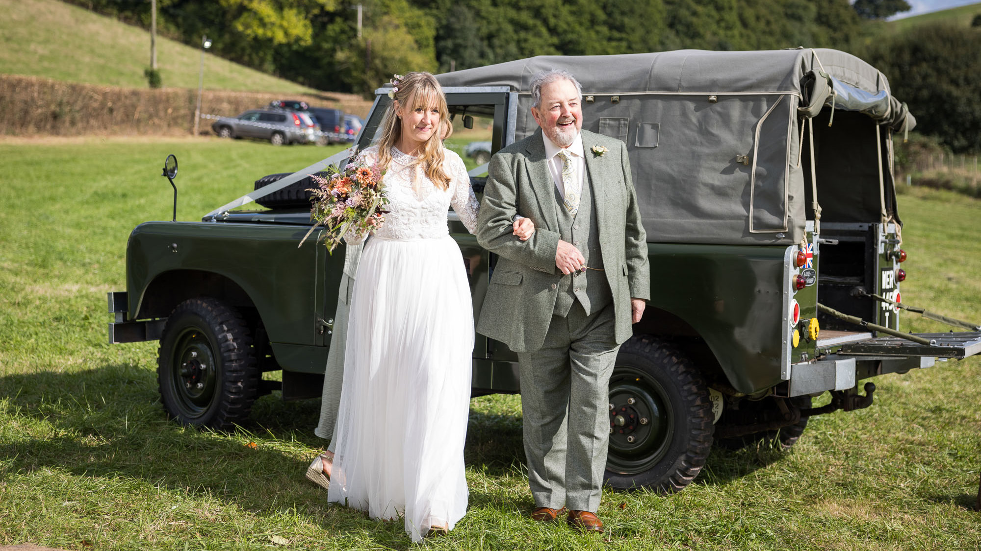 Bride wearing a white dress and her groom in front of a classic Landrover