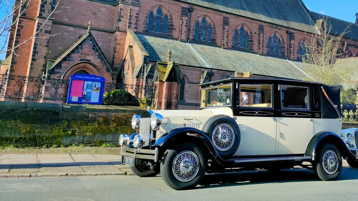 Left side view of a vintage car in Black & Ivory with soft top roof closed parked in front of a Church in Liverpool