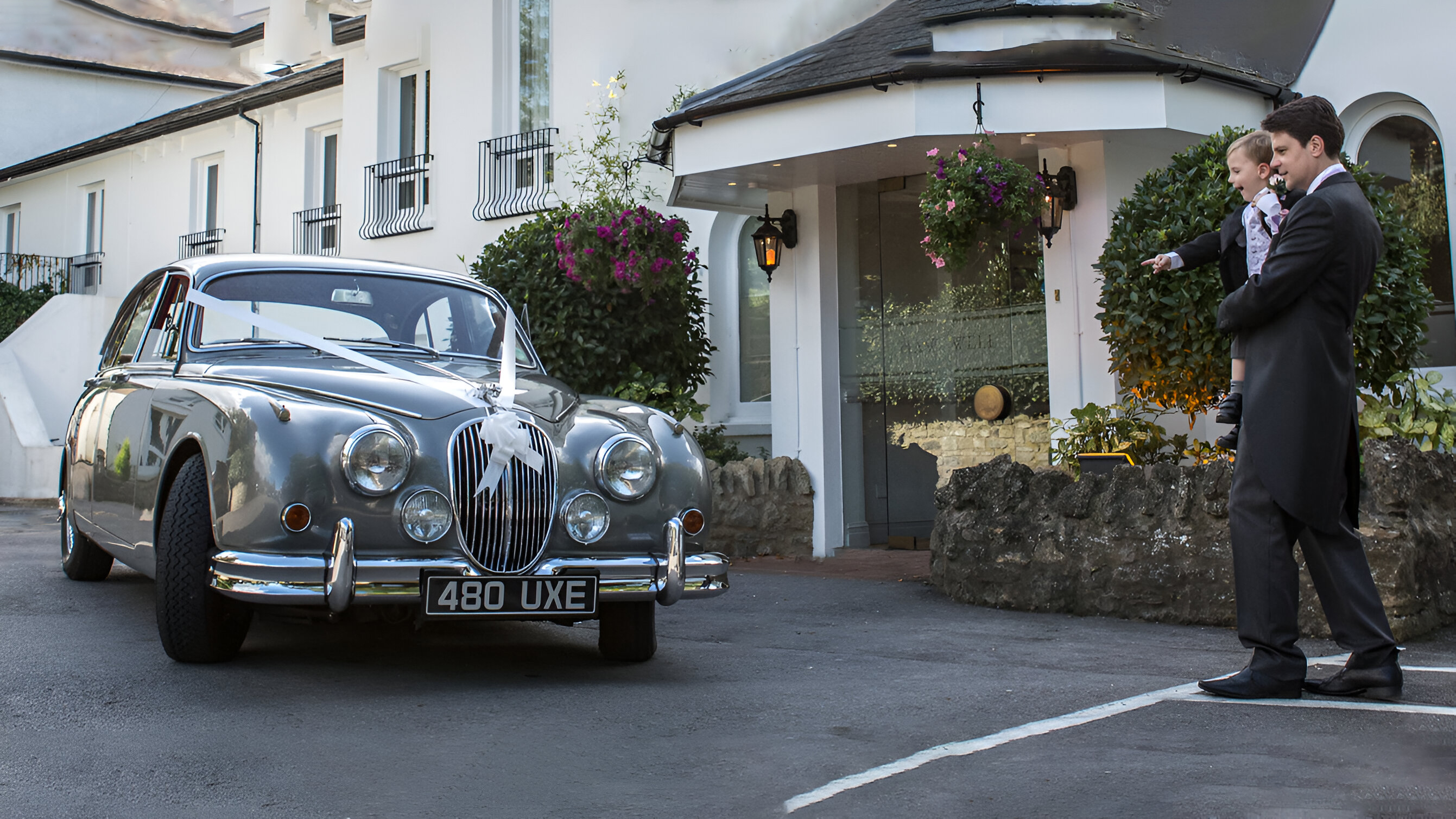 Classic Jaguar Mk2 in silver dressed with white wedding ribbons with Groom holding his little son