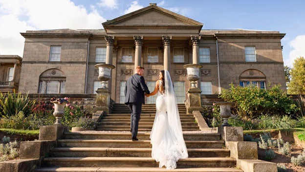 Bride wearing a white wedding dress holding her groom's hand as they walk up the brick stairs at the back of Tatton Park wedding venue