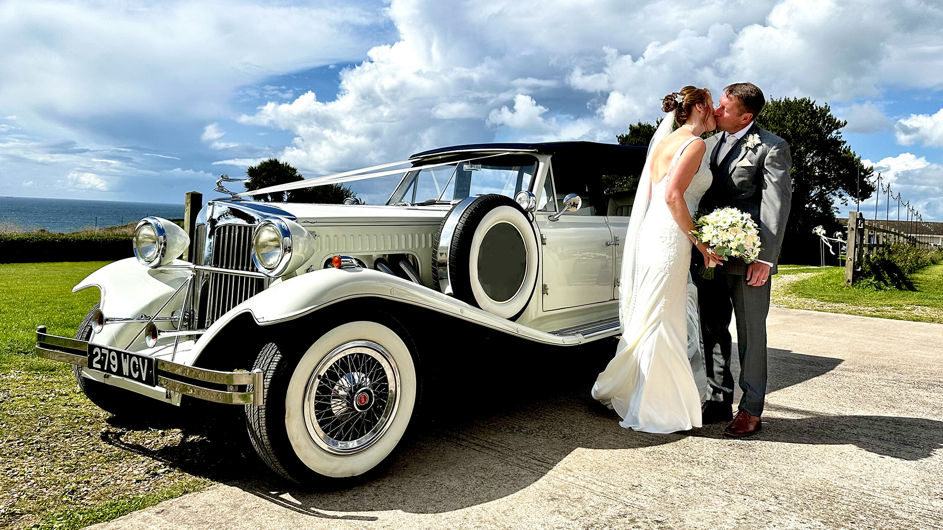 Vintage Beauford convertible parked on Devon's coastline with Bride and Groom kissing