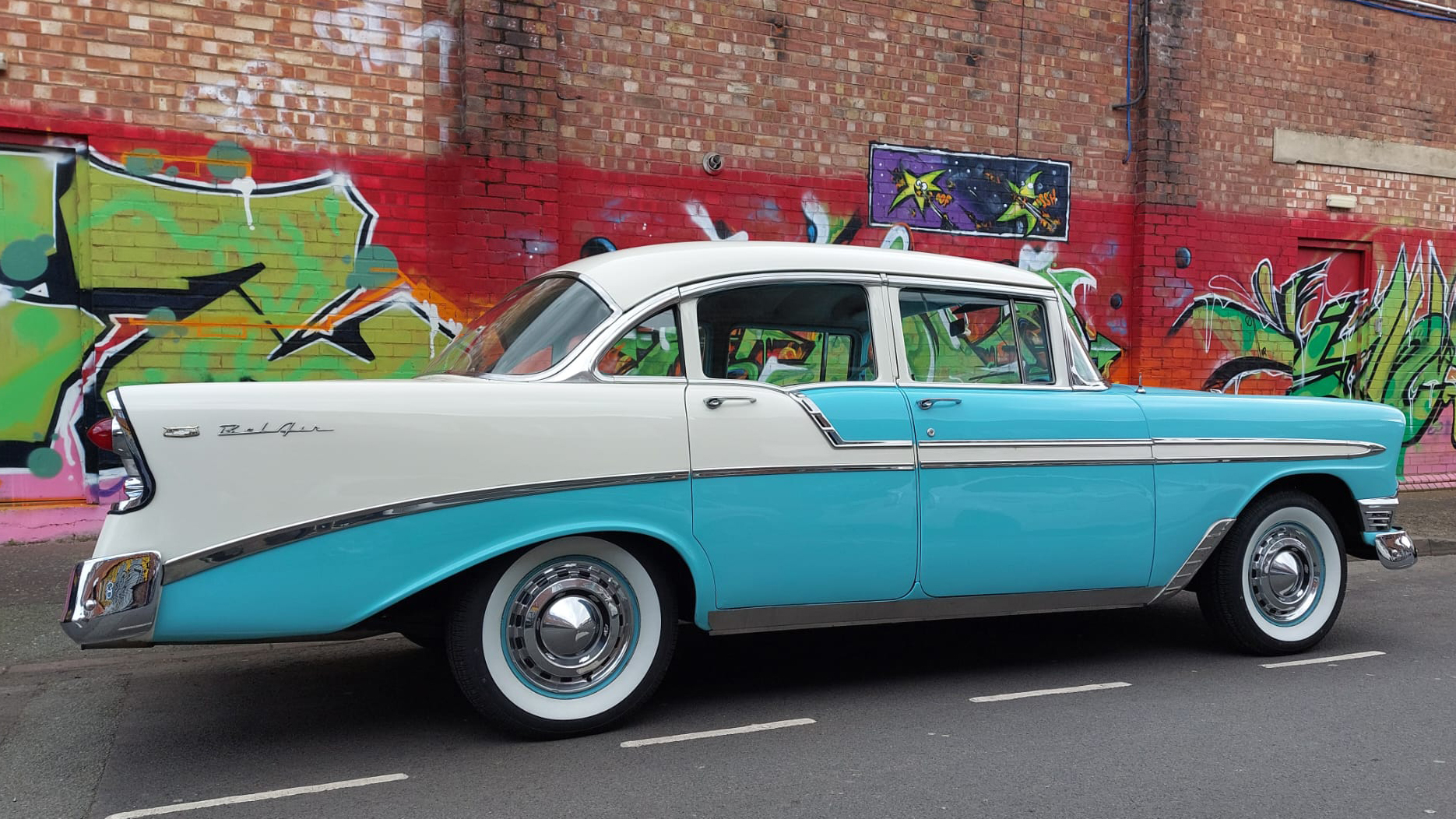 Left rear view of classic American Chevrolet BelAir with painted Artwork on the wall in the background