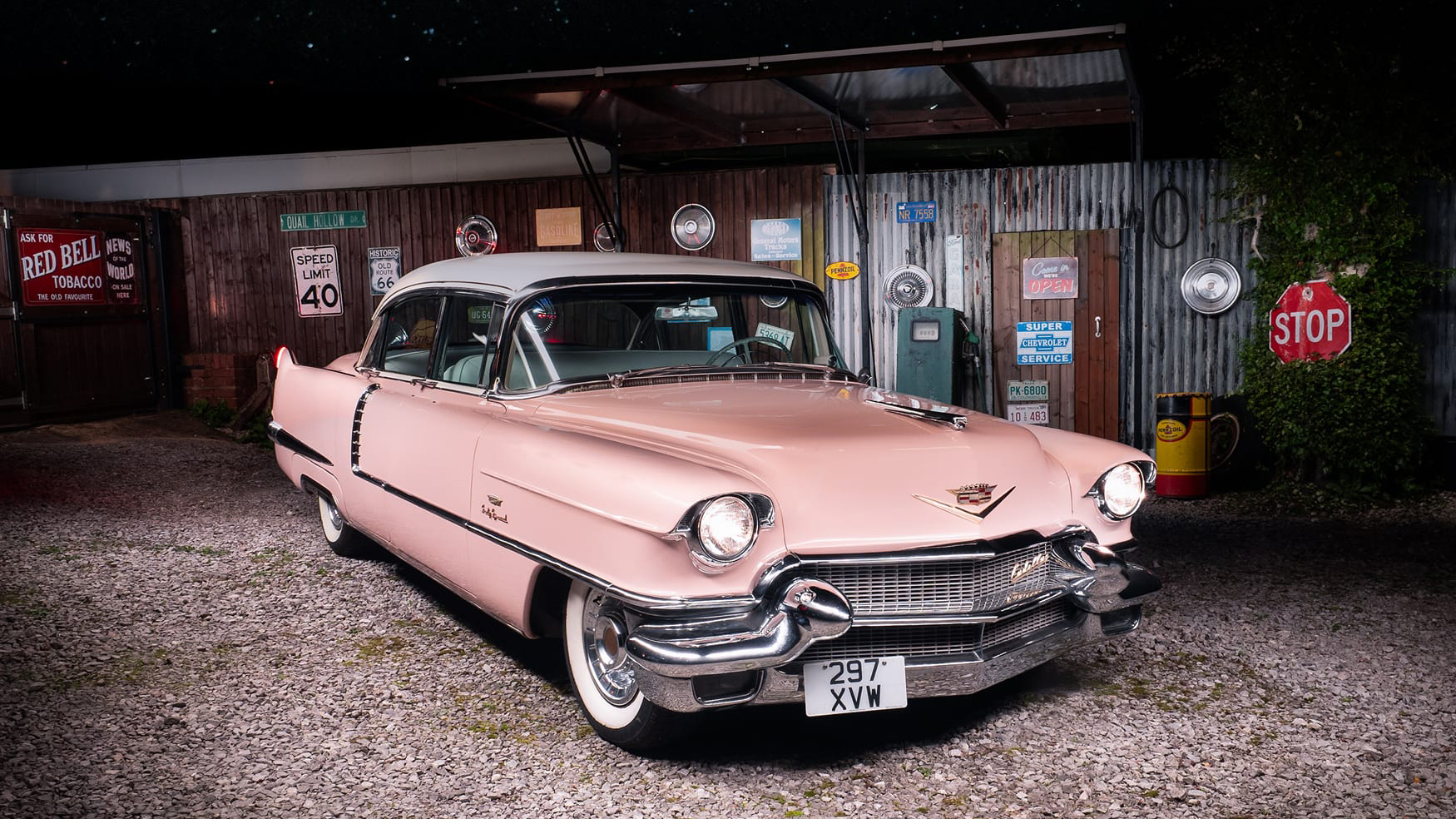 Classic Pink American Cadillac Fleetwood at dusk with headlights on and 50s American ornaments on a wall in the background