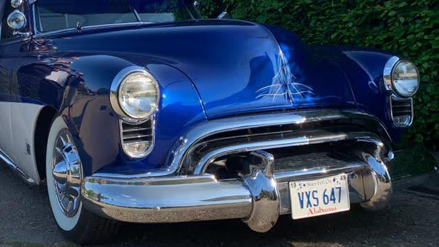 Close-up front view of Oldsmobile Rocket 88 with large chrome bumper and headlights switched on