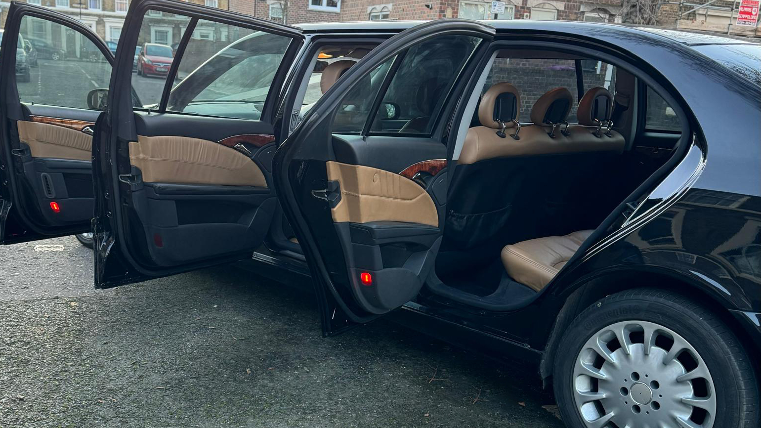 Rear left side view of Mercedes Stretched Limousine with all three doors open showing a black and cream leather interior.