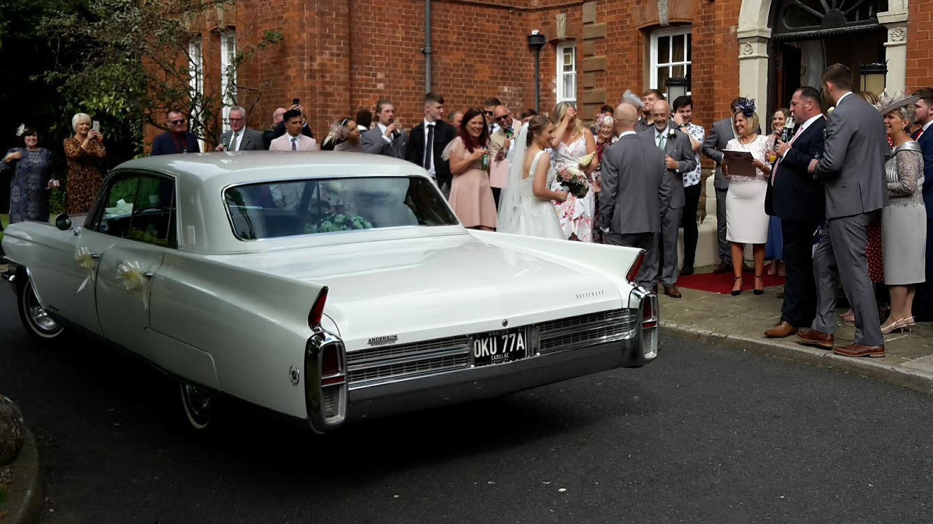 White American Fleetwood parked outside wedding venue with wedding guests in the background