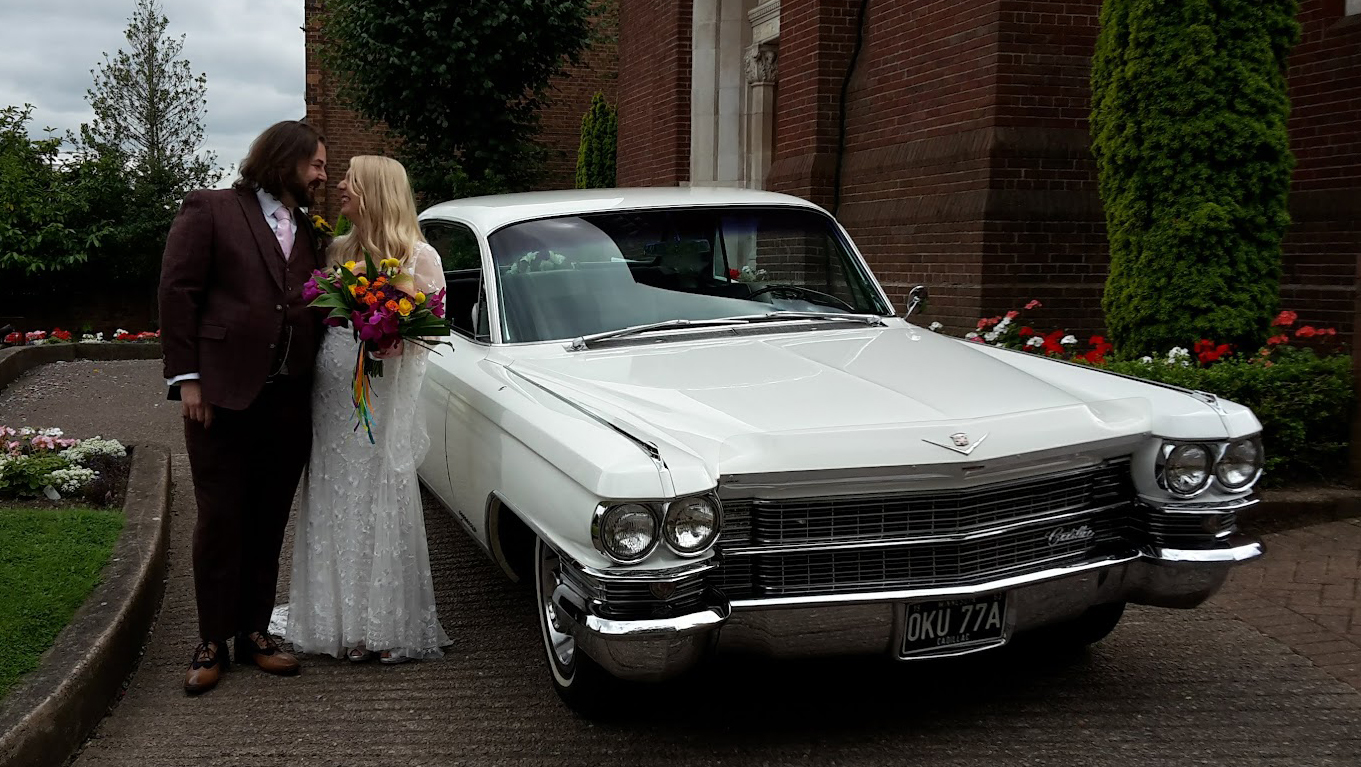 Classic White American Cadillac Fleetwood with Bride and Groom standing by the vehicle kissing