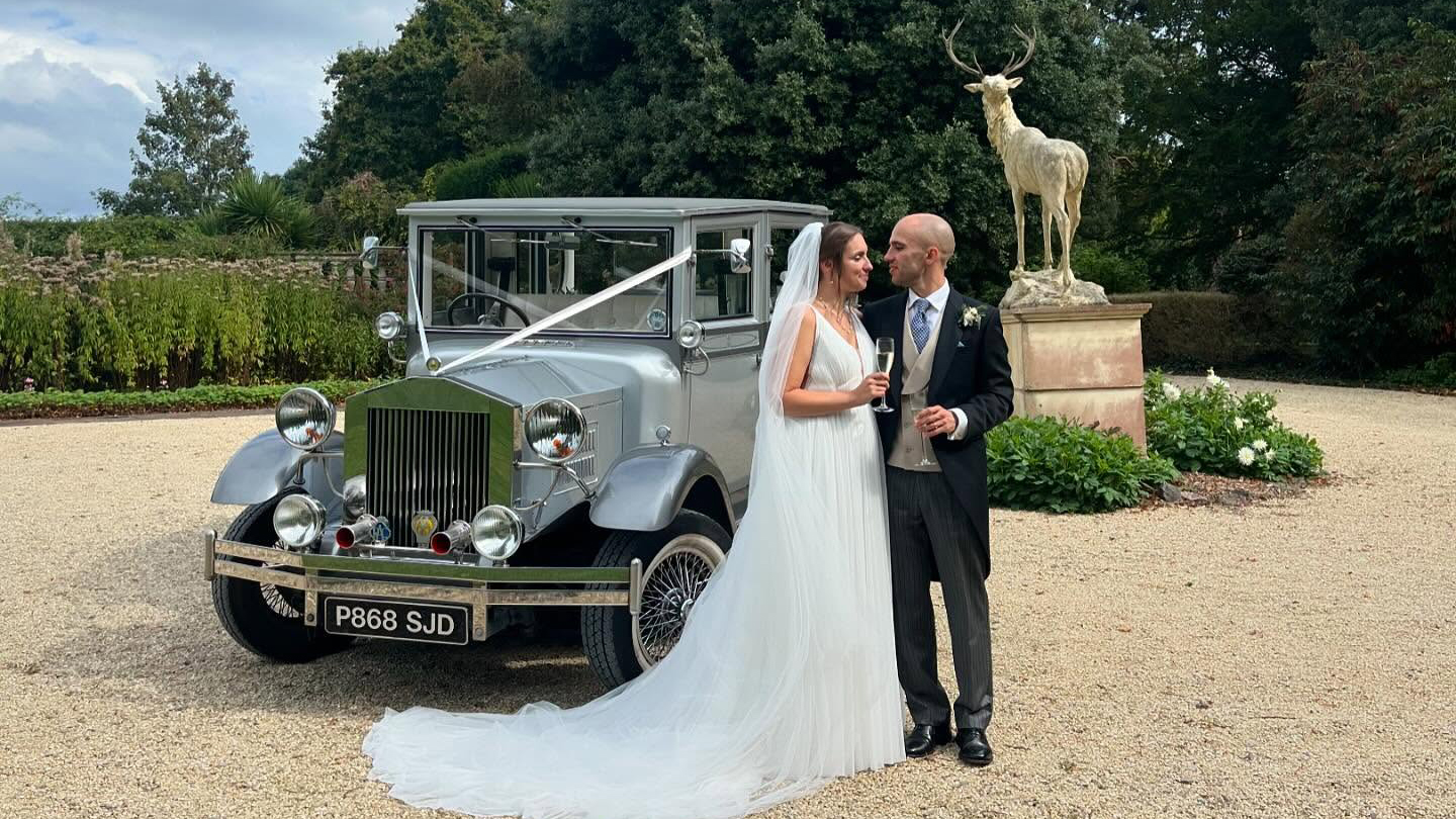 Bride and Groom holding each others in front of a vintage Imperial wedding car