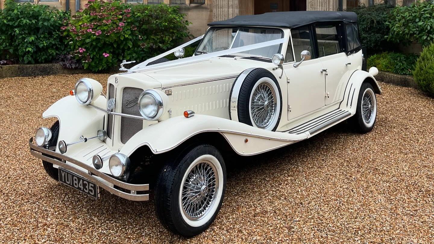 Cream Beauford with black soft top roof closed and decorated with white ribbons parked in front of venue in Bristol