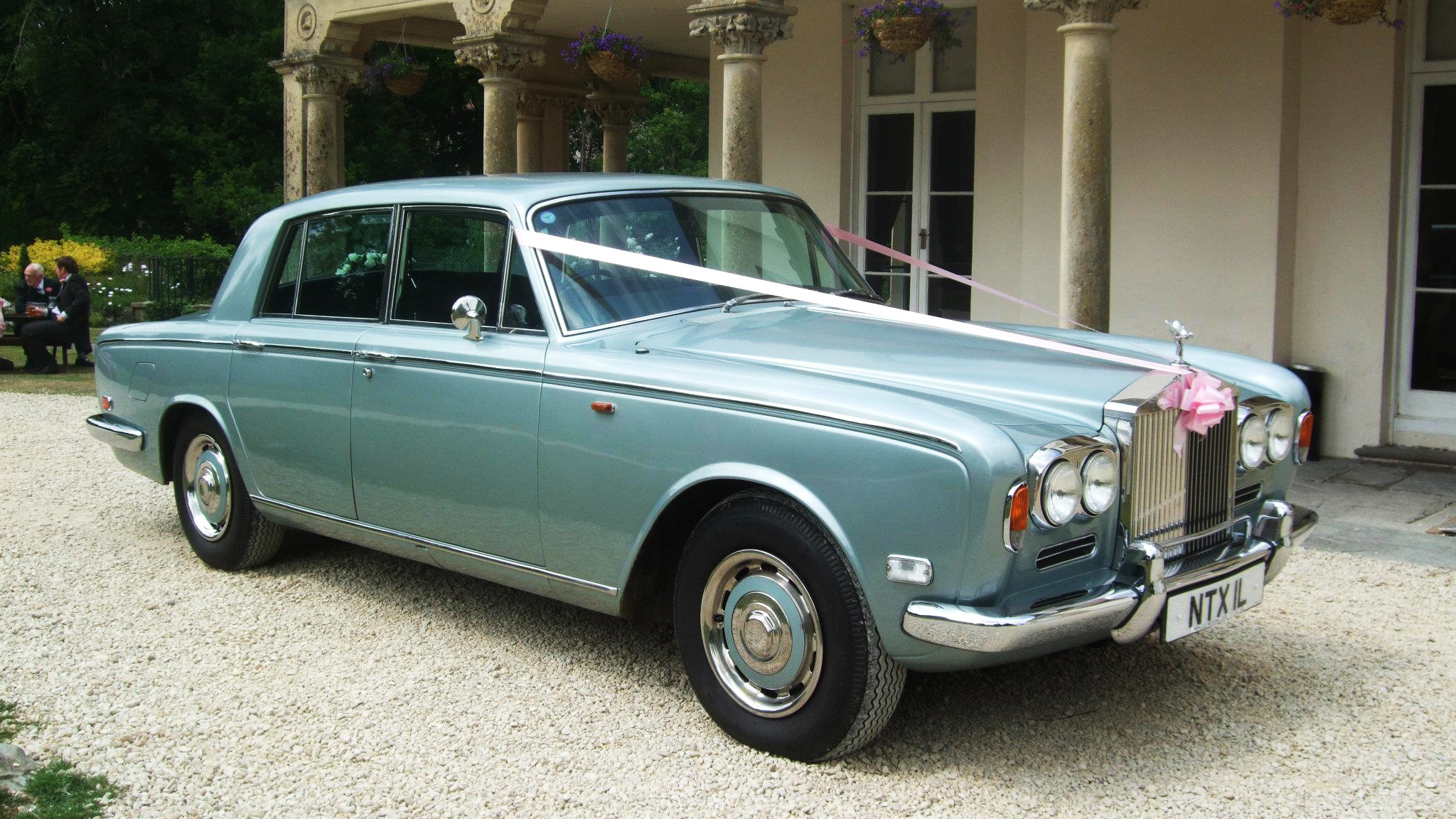 Classic Rolls-Royce Silver Shadow dressed with light pink ribbons and bows in front of a wedding venue in Bristol