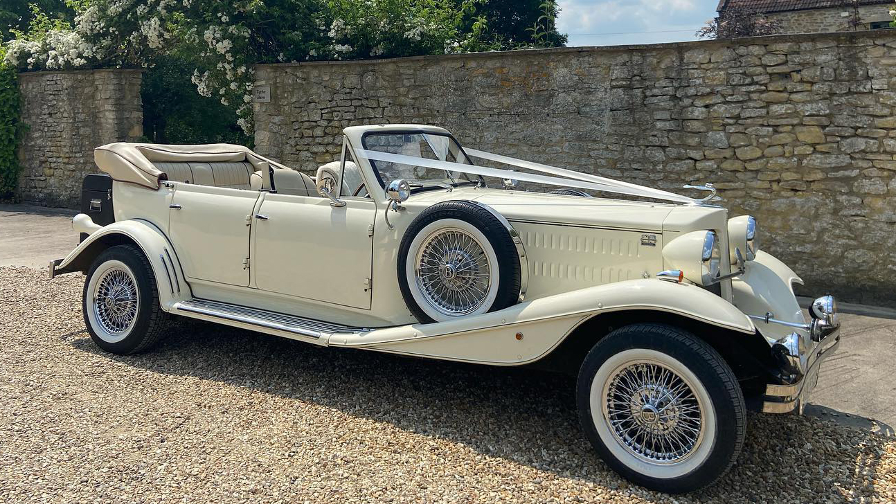 Right side view of cream Beauford with convertible roof open, spokes wheel and spare wheel mounted on the side of the car