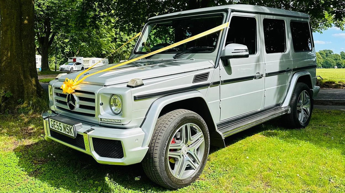 Silver Mercedes G-Wagon decorated with yellow wedding ribbons and bows parked on a green grass