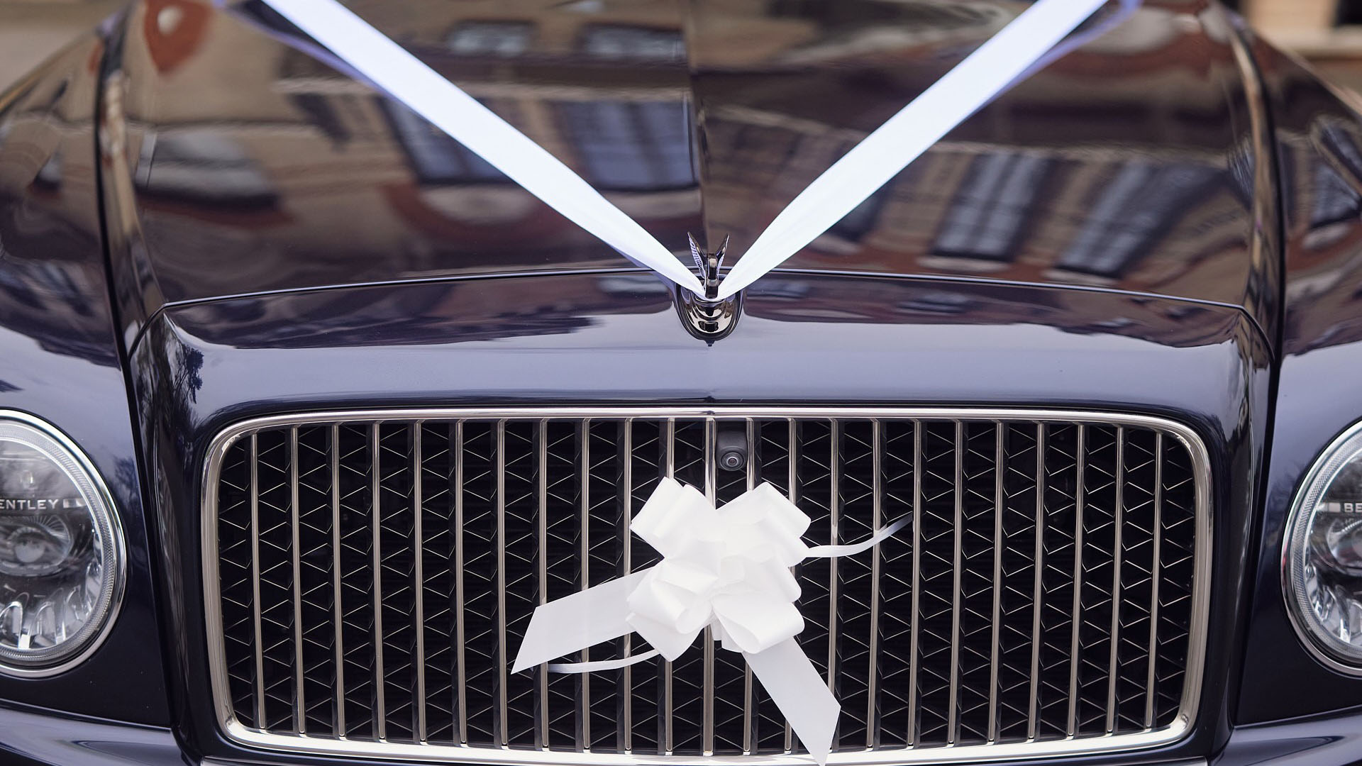 Close-up view of Blue Bentley front grill with white wedding bow and ribbons on the bonnet