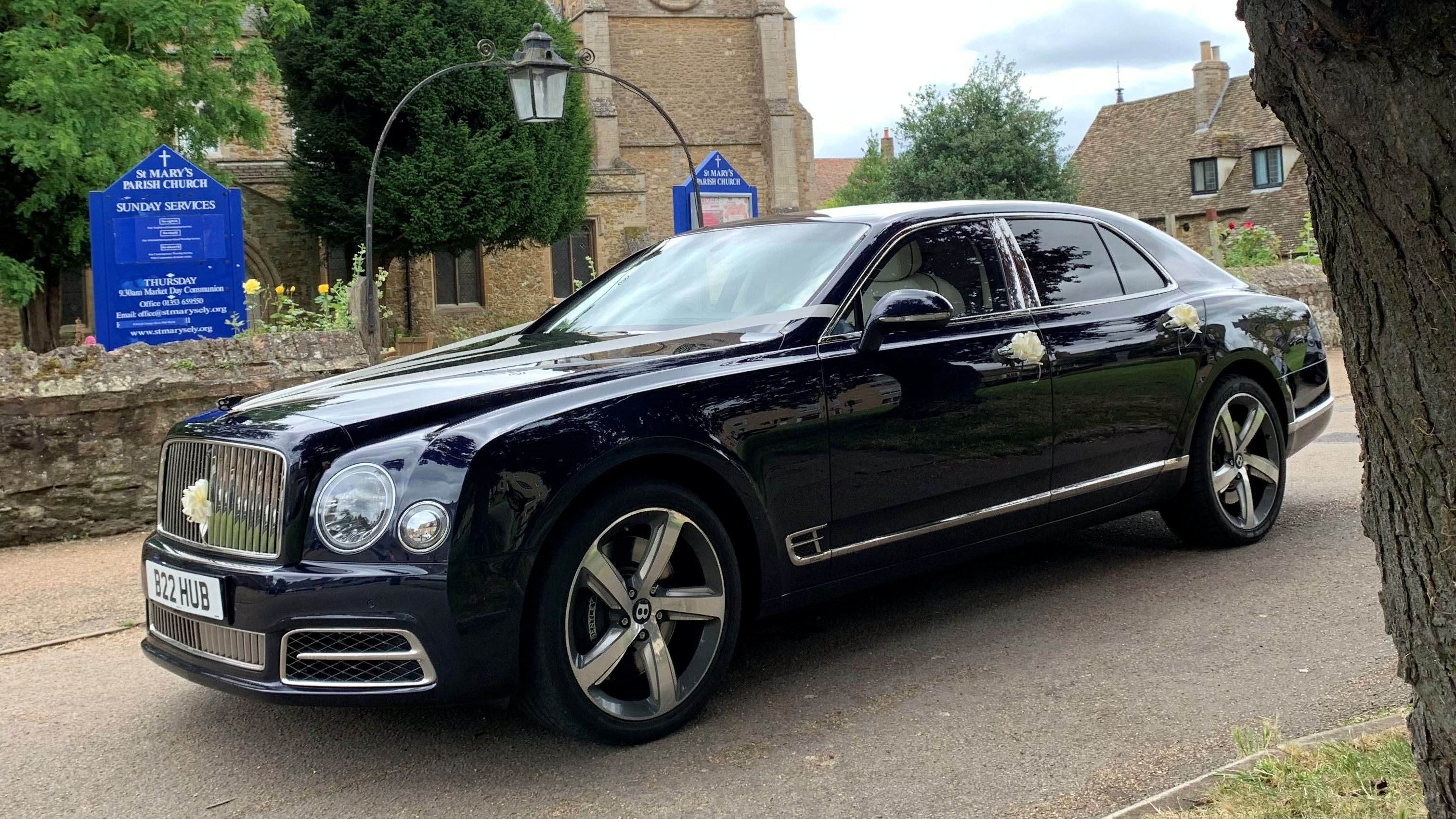 Left side view of a cark blue Bentley Mulsanne with wedding ribbons and bows parked in front of a wedding church